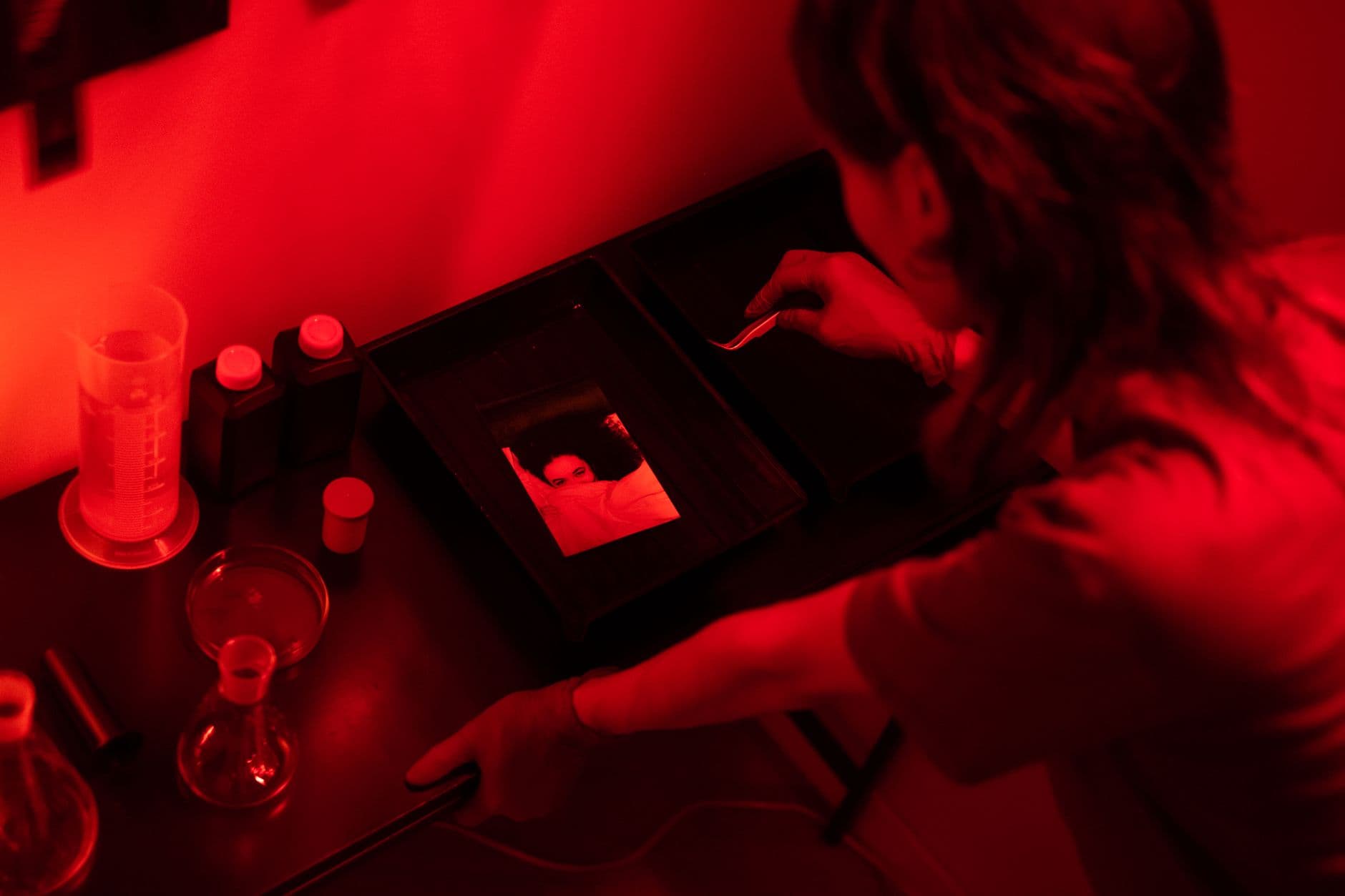 Person working at trays in a darkroom.