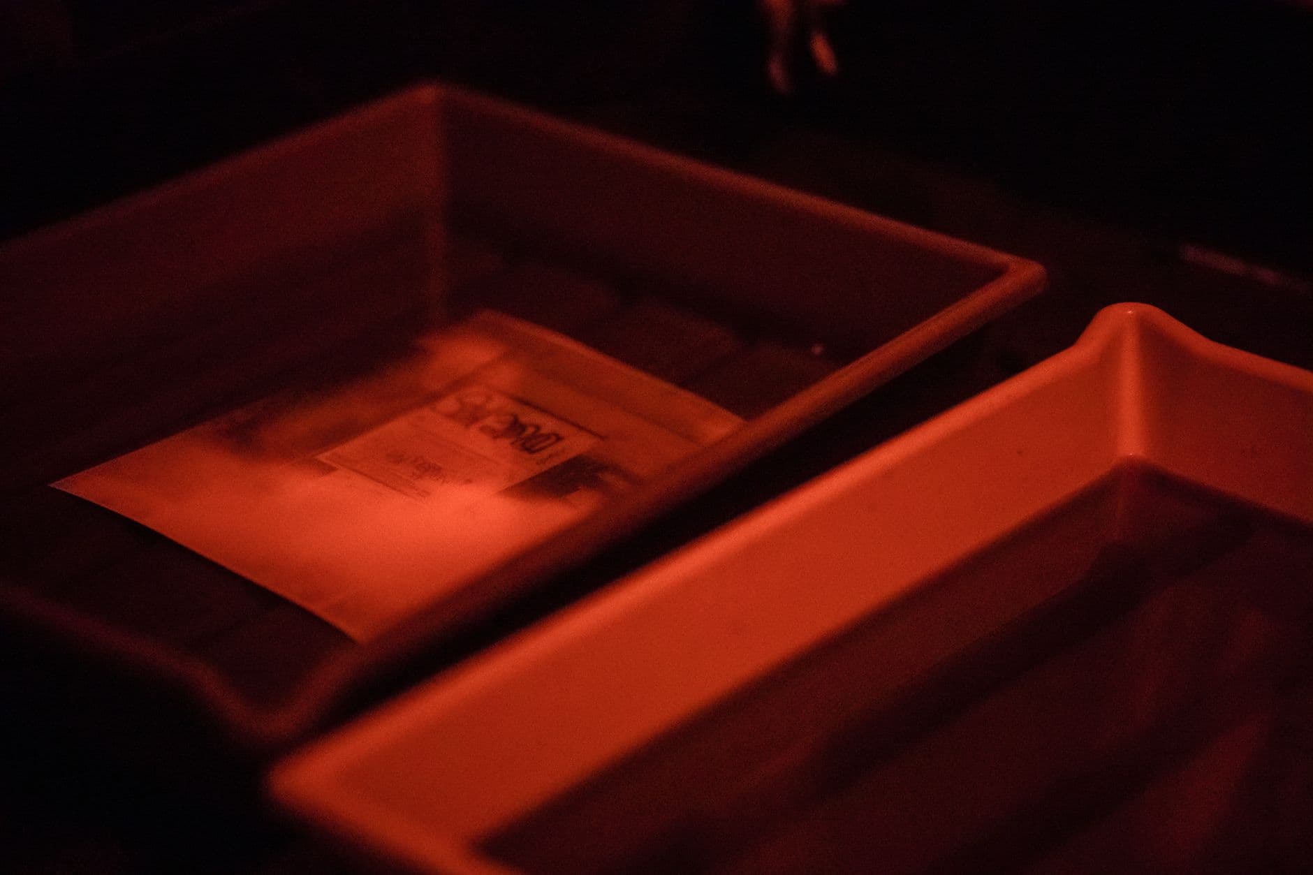 Photographic paper developing in a darkroom tray under red light.
