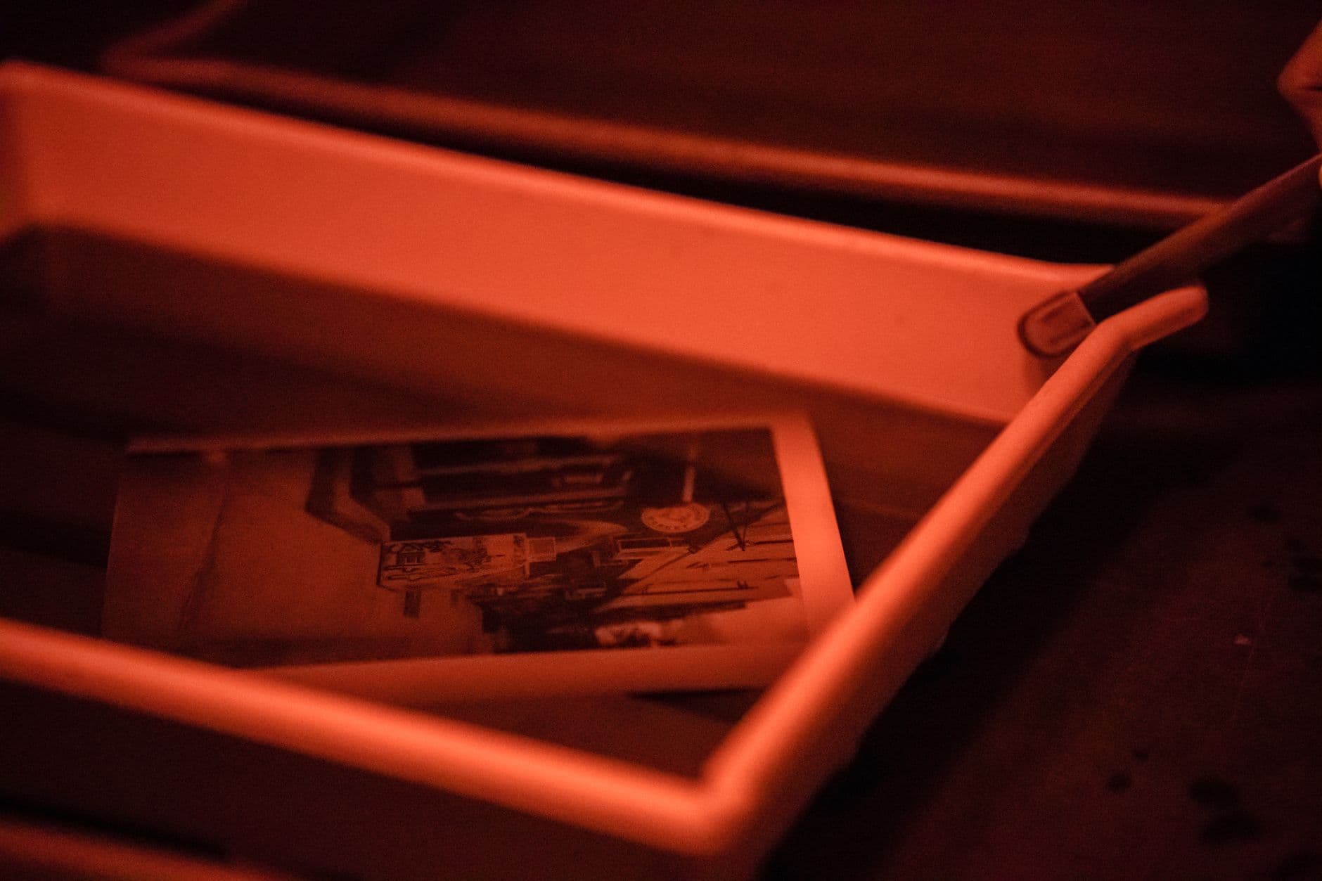 Monochrome photograph developing in a red-lit tray.